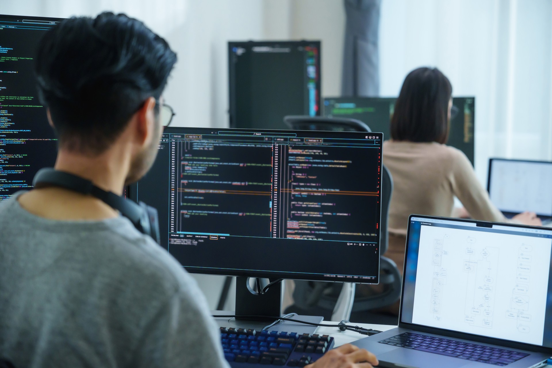 Asian software developers working on multiple screens displaying code and application diagrams in a modern office